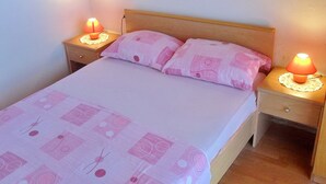 Yhden hengen sänky, jossa on puinen pääty, kaksi yöpöytää lampuineen ja vaaleanpunainen kuviollinen päiväpeite.