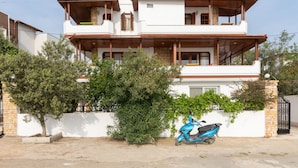 Une maison à deux étages avec un balcon, un scooter garé devant et un mur blanc avec un portail.
