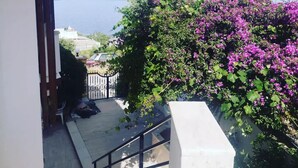 Un balcon avec vue sur la mer, un escalier et un jardin agrémenté de fleurs violettes.