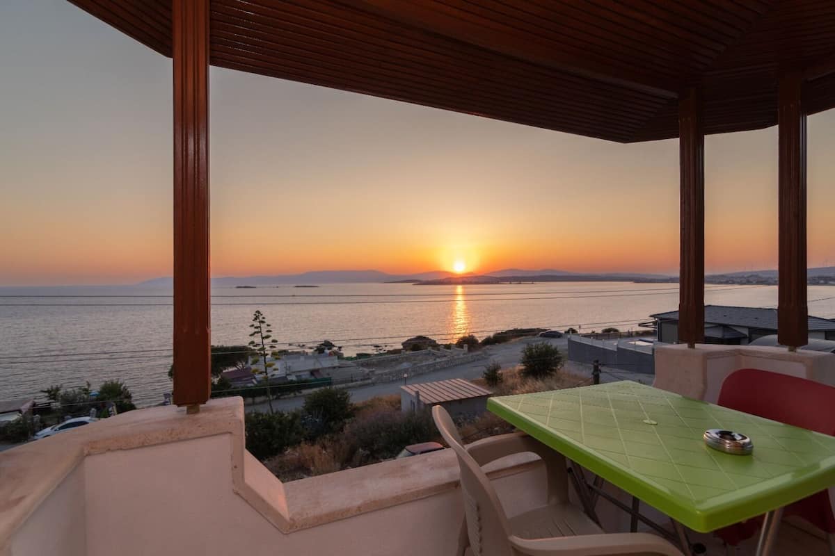 Una terraza con mesa y sillas que da a una vista del atardecer sobre el mar.