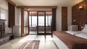 Une chambre d’hôtel avec un lit, une cheminée, une vue à travers une porte vitrée et un mur en pierre.
