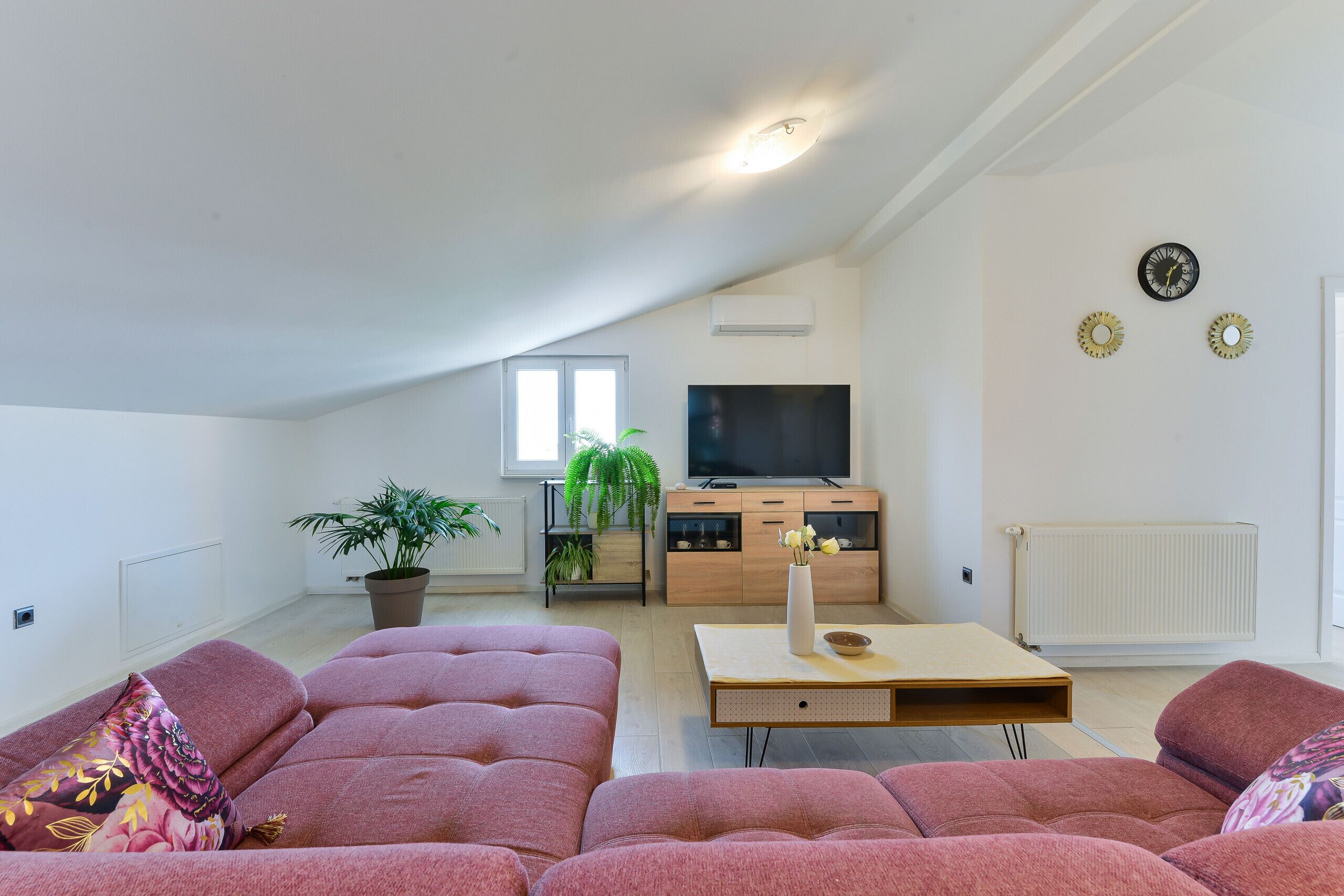 A modern living room with a large sectional sofa, a TV, and a potted plant.