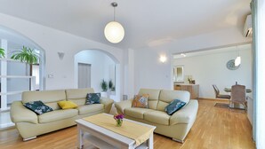 Una sala de estar moderna con dos sofás beige, una mesa de centro blanca y una zona de comedor con una mesa y sillas.