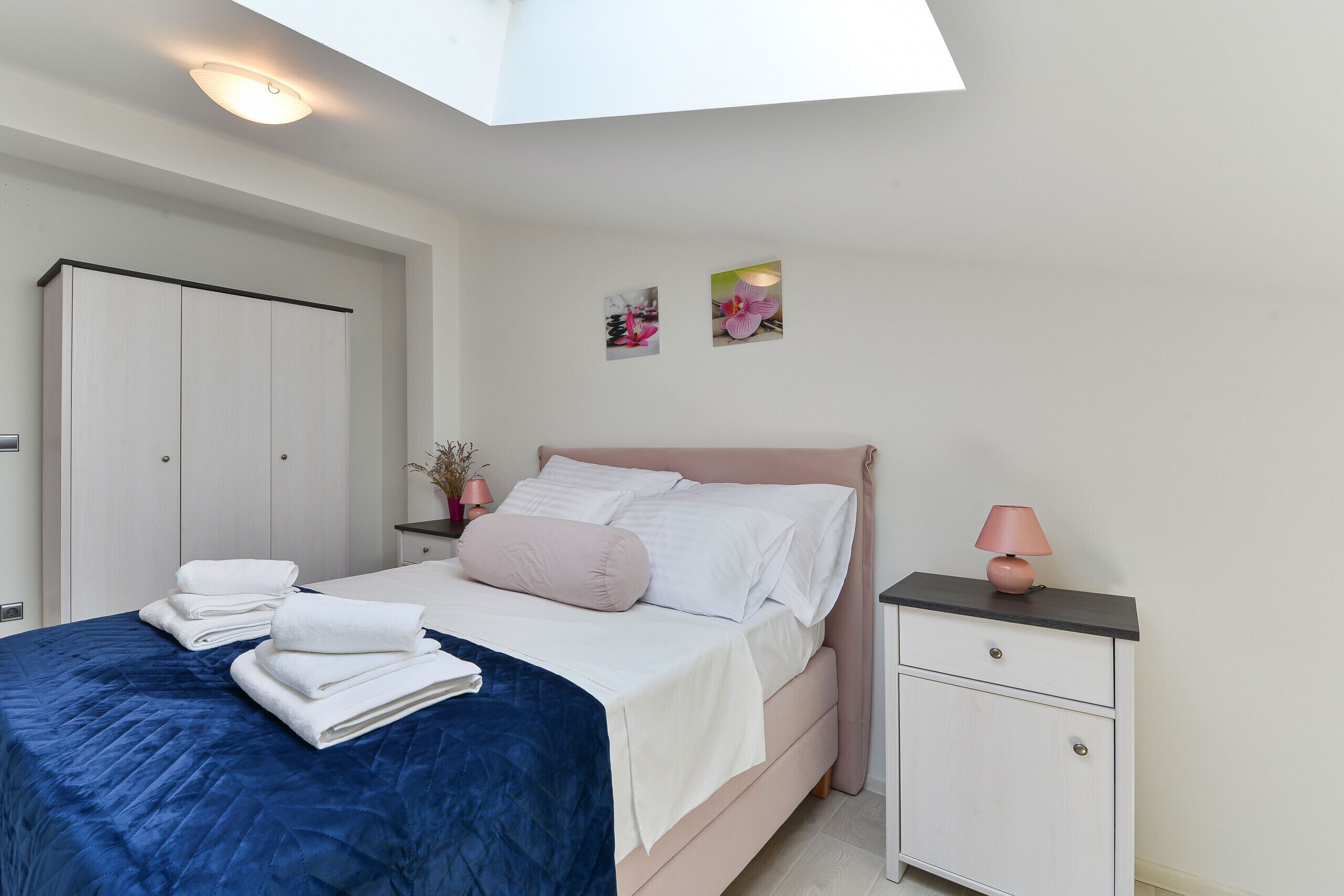 A bedroom with a bed, a nightstand, a wardrobe, and a skylight.