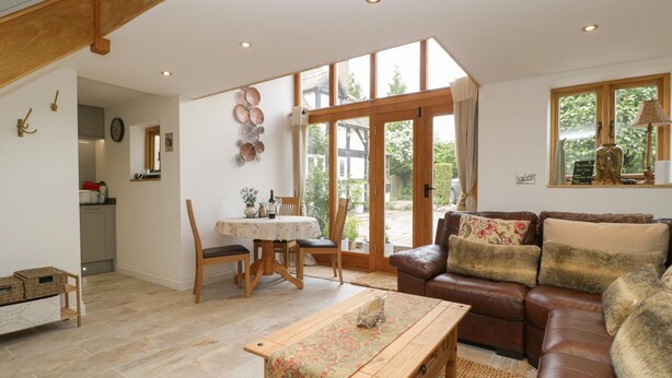 Amplia sala de estar con una mesa de centro de madera, un sofá de cuero marrón y una mesa de comedor con sillas. Una ventana grande ofrece luz natural y vistas al exterior.