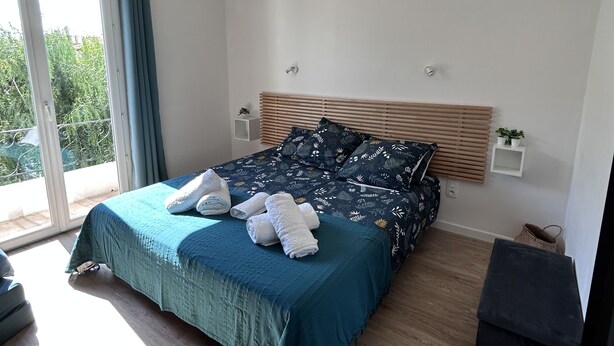 A modern bedroom with a large bed, a ceiling fan, and a view of greenery outside. - Superb upstairs villa with private garden and parking. (Saint-laurent-du-var)