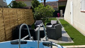 An outdoor swimming pool with a ladder, surrounded by a wooden fence, a palm tree, and outdoor furniture. - Superb upstairs villa with private garden and parking. (Saint-laurent-du-var)