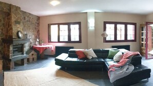 Una sala de estar con una pared de piedra, un sofá negro y una mesa roja con un reloj.