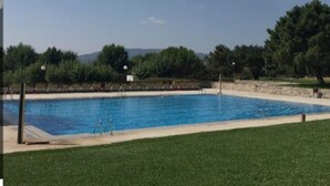 Una piscina rectangular con agua azul cristalina, rodeada por un muro de piedra y una zona ajardinada.