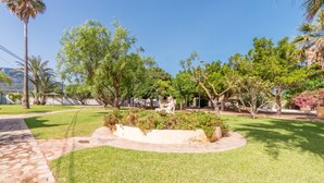 A landscaped garden with a stone pathway, various trees, and a central planter area. - "El Cid" Holiday Apartment with Sea View, Pool, Garden & Terrace (Denia)
