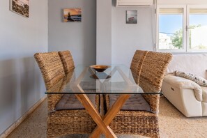 A room with a glass-top table, wicker chairs, a cushioned sofa, and artwork on the walls.