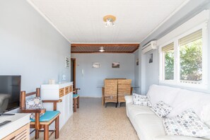 A room with a TV, wooden furniture, a white sofa, and a dining area.