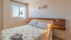 A bedroom with a bed, a window, a headboard, and a wall-mounted light fixture. - "El Cid" Holiday Apartment with Sea View, Pool, Garden & Terrace (Denia)