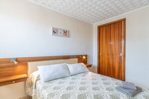 A bedroom with a wooden headboard, a bed with a patterned bedspread, a nightstand with a lamp, and a wooden wardrobe.