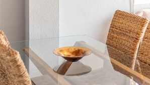 A glass table with a woven basket centerpiece, surrounded by woven chairs. - "El Cid" Holiday Apartment with Sea View, Pool, Garden & Terrace (Denia)
