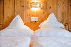 Un lit double avec une literie blanche et deux oreillers, une tête de lit en bois et un luminaire fixé au mur.