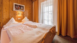 A double bed with white linens, a wooden headboard, a wall-mounted light, and a window with curtains. - Holiday Apartment 'Schwalbennest' with Mountain View, Wi-Fi, Balcony and Garden (Mühlbach)