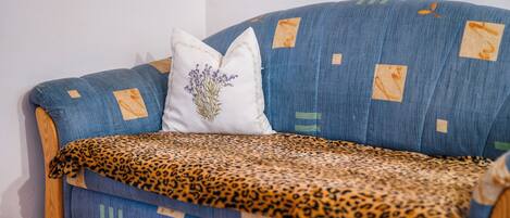 Un sofá azul con un plaid de estampado de leopardo, una almohada blanca con diseño floral y un marco de madera.