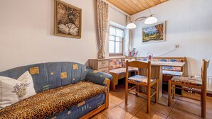 A cozy room with a sofa, a dining table with chairs, a window with curtains, and two wall-mounted lamps. - Holiday Apartment 'Schwalbennest' with Mountain View, Wi-Fi, Balcony and Garden (Mühlbach)
