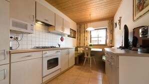 A kitchen with white cabinets, a stove, a microwave, and a dining area with a chair and table.
