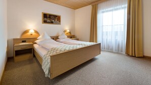 A bedroom with a wooden bed, two bedside tables with lamps, a painting on the wall, and a large window with curtains.