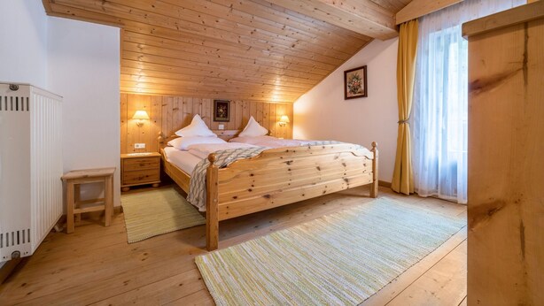 A wooden-paneled bedroom with a bed, nightstands, a radiator, and a window with curtains. - Holiday Apartment "Waldesruh" with Mountain View, Balcony & Wi-Fi (Mühlbach)