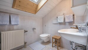 Een badkamer met dakraam, toilet, wastafel en handdoeken aan de muur.