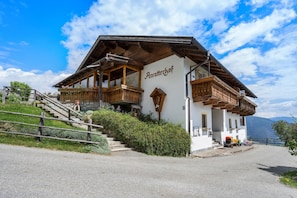 A traditional wooden building with a balcony, a staircase leading to the entrance, and a view of the surrounding landscape.