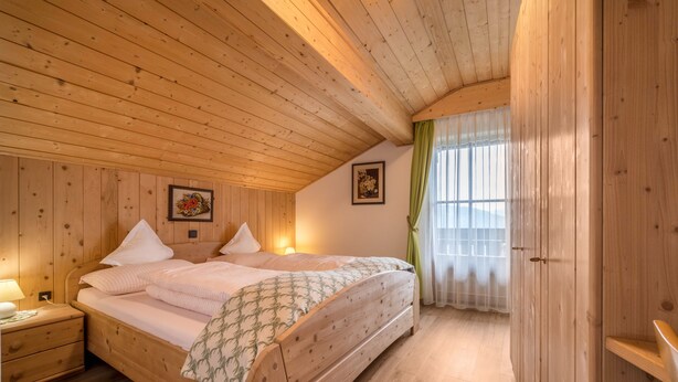 Een kamer met houten vloer, een bed, nachtkastjes en een raam met gordijnen.
