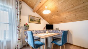 Een eethoek met een houten tafel, blauwe stoelen met bekleding, een schilderij aan de muur en een plafondlamp.
