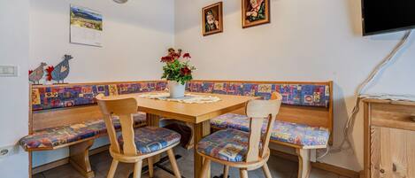Un coin repas comprenant une table en bois, quatre chaises, un banc, une horloge et deux tableaux encadrés accrochés au mur.