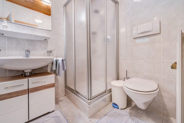 Une salle de bain moderne équipée d’un lavabo, d’un miroir, d’une douche, de toilettes et de meubles de rangement.