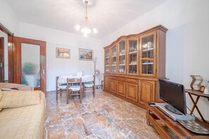 A room with a bed, a dining table with chairs, a wooden cabinet with glass doors, a television, and a ceiling fan.