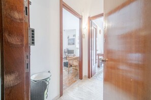 A hallway with a wooden door, a trash bin, and a wicker chair.