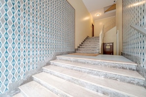 A staircase with a patterned wall, a wooden door at the top, and a handrail on the right.