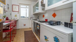 Ett modernt kök med vita skåp, en gasspis, en diskmaskin och en röd stol.