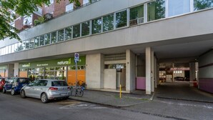 En byggnad med en grön skylt där det står ”naturasi” och en parkeringsplats med bilar och cyklar.