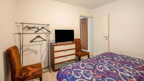 Quarto com cama, cômoda, televisão por cima, cadeira e um cabideiro.