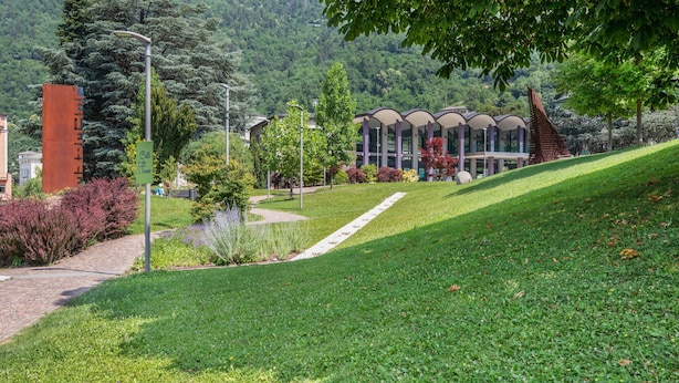 Uma área ajardinada com um caminho que leva a um edifício moderno e uma estrutura de telhado singular.