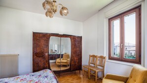 Een slaapkamer met een bed, een garderobe, een stoel, een raam en een spiegel.