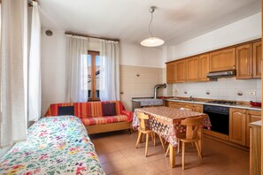 A compact kitchen with wooden cabinets, a dining table with chairs, a sofa, and a window with curtains.