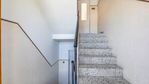 Een trap met een leuning, een deur aan de bovenkant, en een muur met een structuurafwerking.