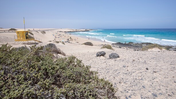 En strand med en redningsplatform, sandklitter og klippeudspring.