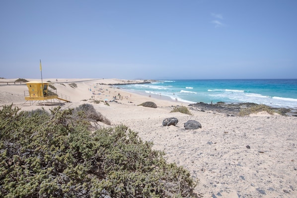 A beach with a lifeguard tower, sandy dunes, and rocky outcrops.