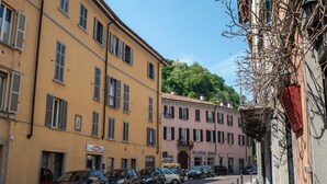 A street with parked cars and buildings, including a yellow building with shutters and a pink building with a sign. - GuestHost - Cozy, completely renovated 47sqm apartment located on the 3rd floor of a building WITHOUT elevator. The apartment is accessed via an external balcony overlooking the quiet internal courtyard.The accommodation is located in an excellent locati (Como)