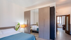 A bedroom with a bed, bedside lamp, and a wardrobe with a mirror. - GuestHost - Cozy, completely renovated 47sqm apartment located on the 3rd floor of a building WITHOUT elevator. The apartment is accessed via an external balcony overlooking the quiet internal courtyard.The accommodation is located in an excellent locati (Como)