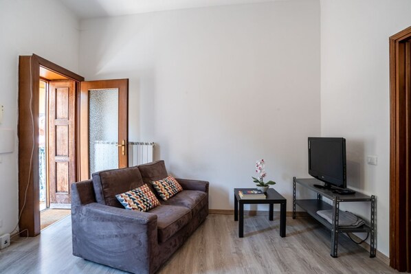 A living room with a brown sofa, a small table with a plant, and a TV on a stand.