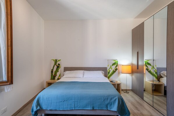 Quarto com cama, luminárias de cabeceira, espelho e planta.