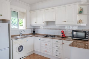 A kitchen with white cabinets, a washing machine, a sink, a stove, a red coffee maker, and a microwave.