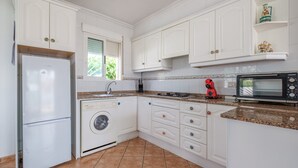 A kitchen with white cabinets, a washing machine, a microwave, and a red toaster.
